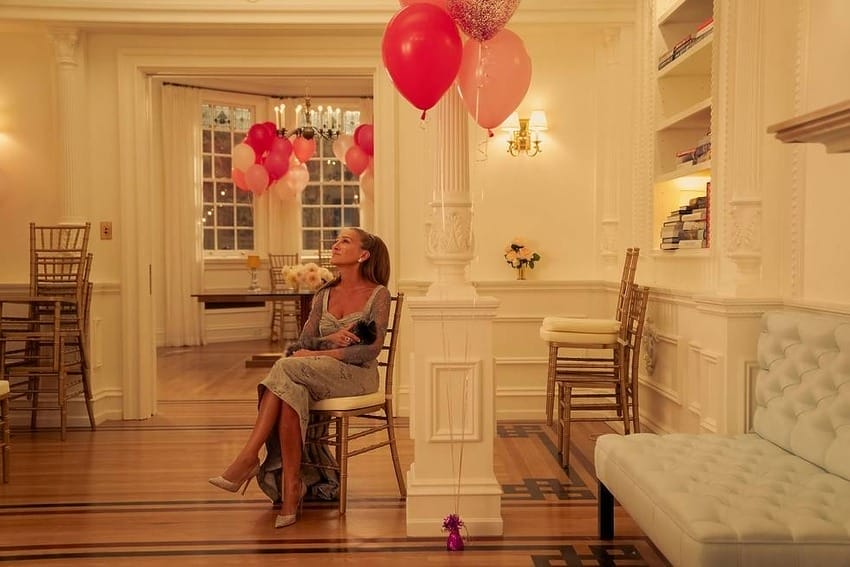 Woman sitting on a chair in a decorated room with pink balloons and dim lighting.