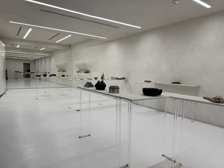 Minimalist gallery with modern sculptures displayed on sleek tables along a white, well-lit corridor.
