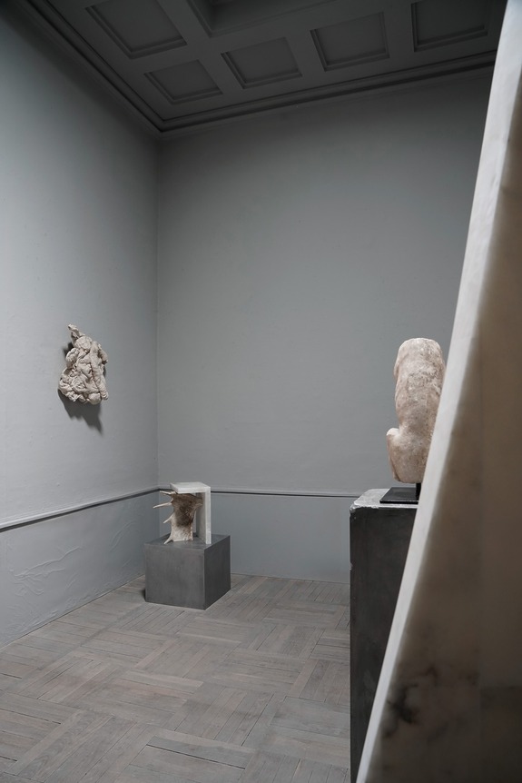 Minimalist gallery space with marble sculptures on pedestals and a wall-mounted relief, featuring a modern aesthetic.