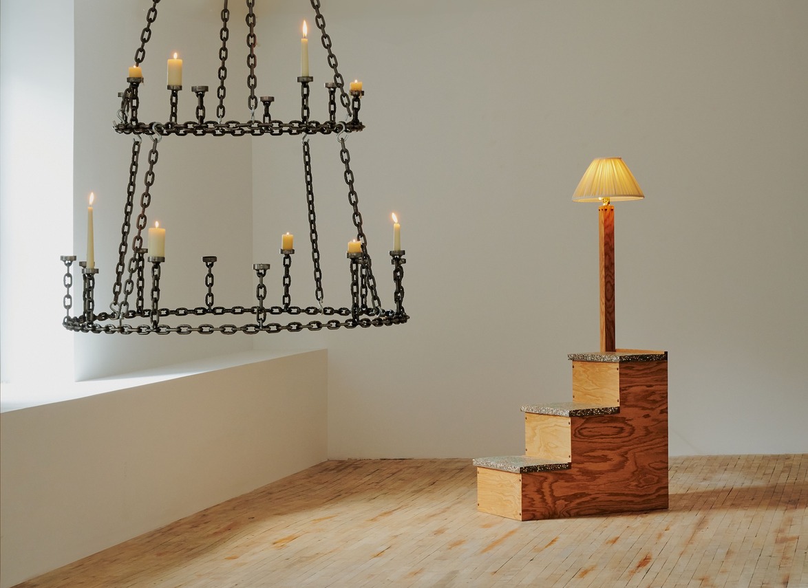 Large candle chandelier and a steps-like wooden lamp in a minimalist room with wooden floorboards.