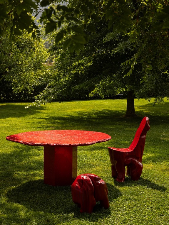 Red wooden table and chairs set on lush green grass under a tree, creating a vibrant contrast.