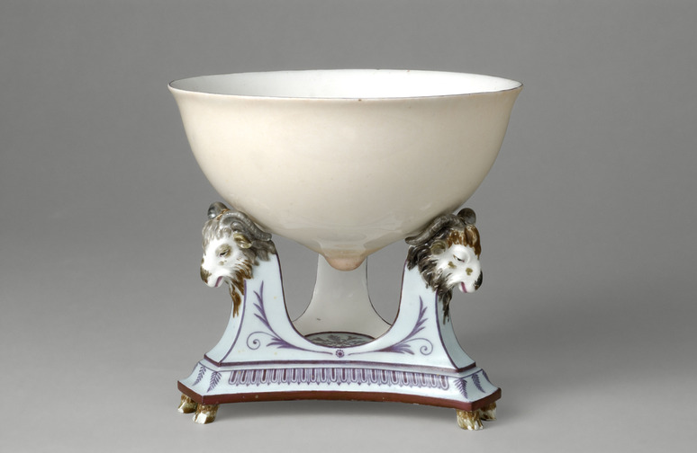 Porcelain bowl with lion head decorations on an ornate triangular base against a neutral background.