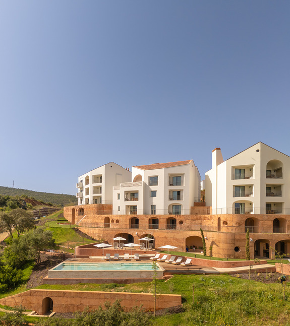 Luxury resort with modern white architecture, multiple balconies, outdoor pool, and sun loungers surrounded by greenery.