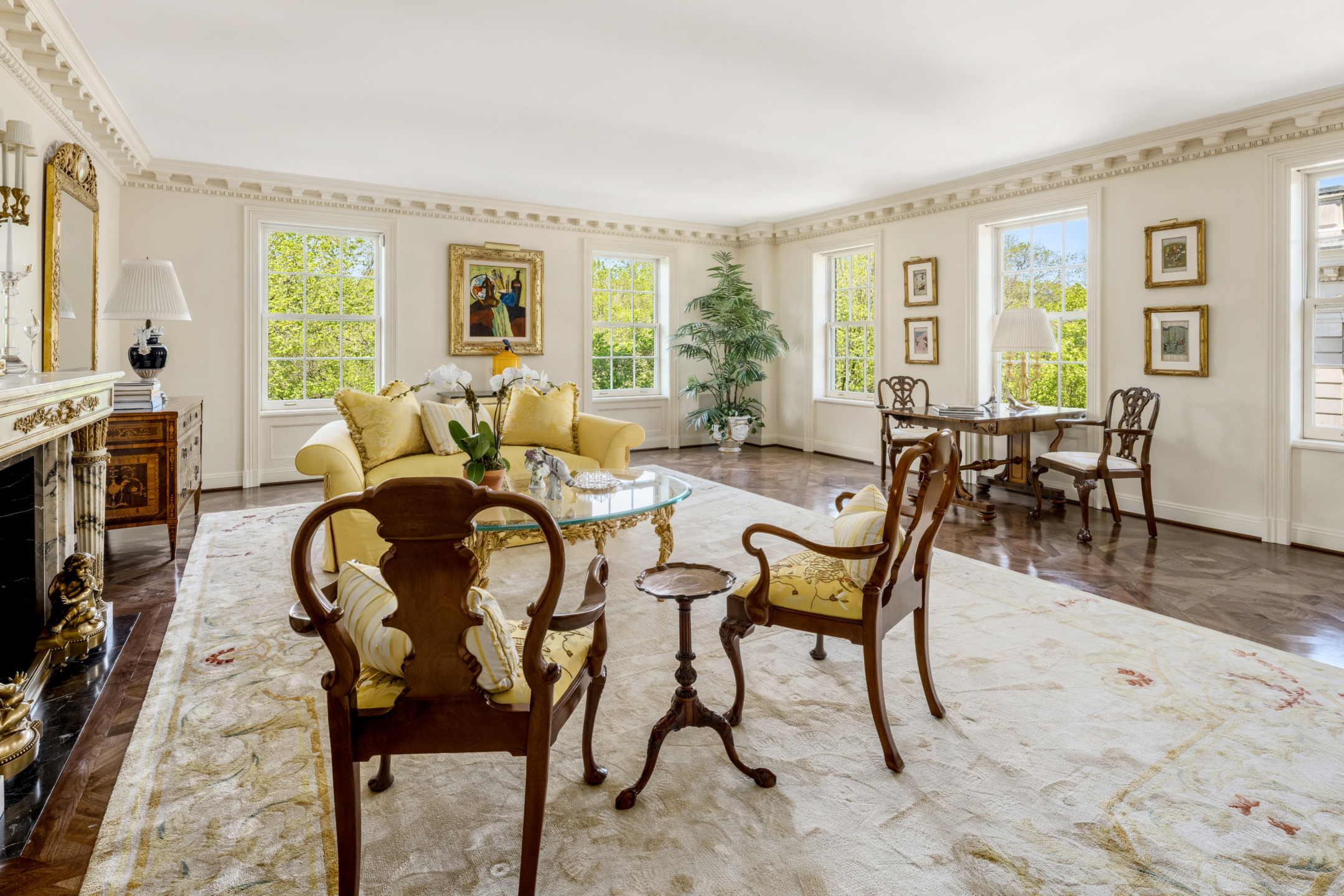 Elegant living room with classic furniture, large windows, decorative moldings, and a fireplace, bathed in natural light.
