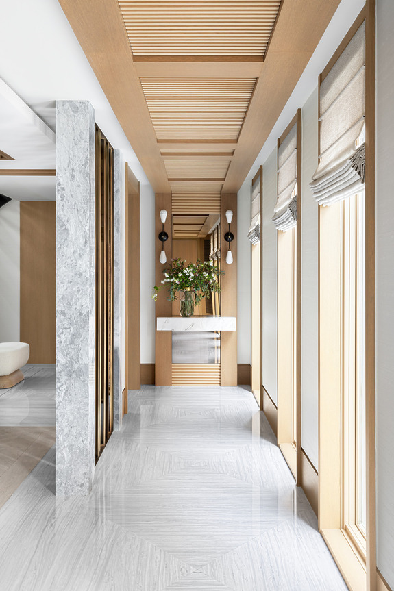 Modern hallway with wooden accents, marble floor, vertical windows, and a decorative console table with a floral arrangement.