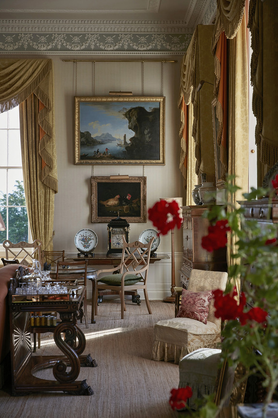 Elegant room with antique furniture, decorative plates, paintings on walls, and vibrant red flowers in the foreground.