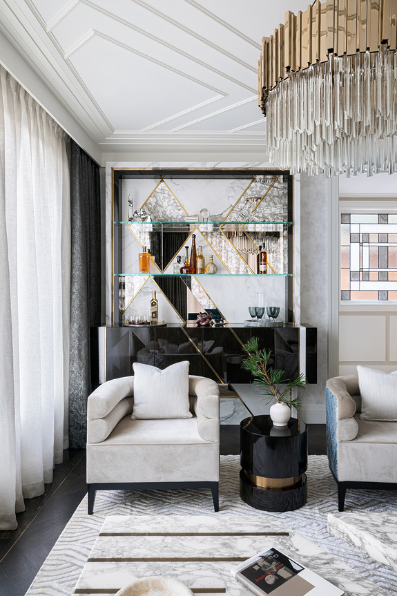 Luxurious modern living room with plush armchairs, marble table, geometric bookshelf, and elegant chandelier.