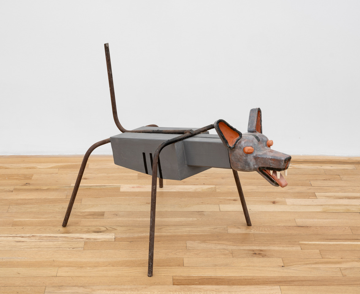 Sculpture of a dog made from metal rods and wood on a wooden floor with a white background.