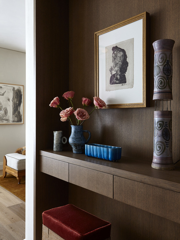 Shelf with pink flowers in a vase, framed art, and decorative pottery in a modern living room setting.