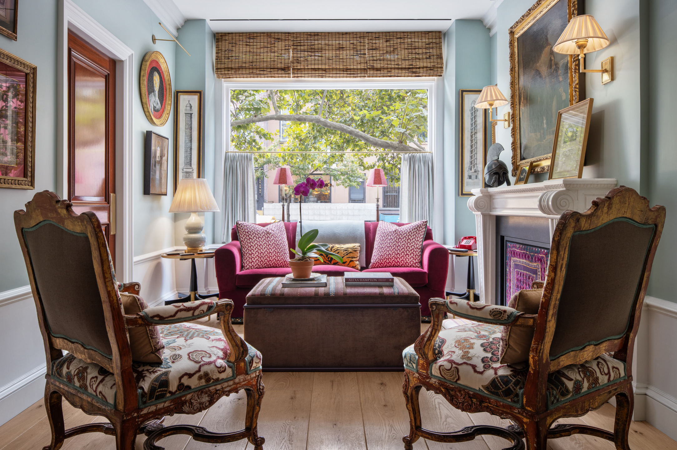 Elegant living room with vintage chairs, ornate fireplace, and large window with view of trees.