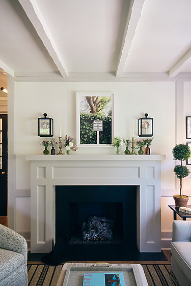 Elegant living room with a white fireplace, black lanterns, a framed picture above, and a cozy seating area.
