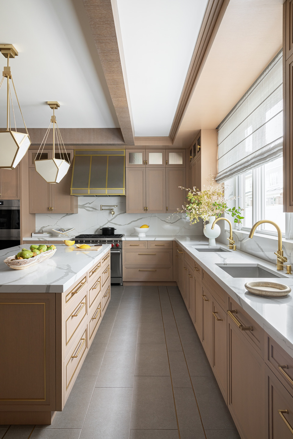 Modern kitchen with wooden cabinets, marble countertops, gold fixtures, and large window with natural light.