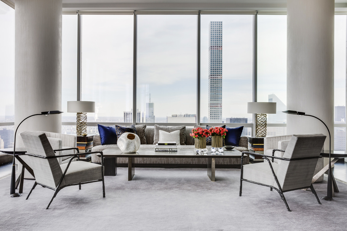 Modern living room with large windows, sleek furniture, decorative pillows, and vibrant flowers on a central coffee table.