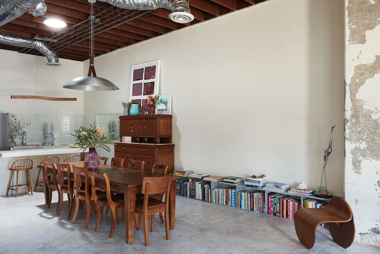 Eclectic dining room with wooden furniture, bookshelves, large table, vintage chairs, and industrial ceiling elements.