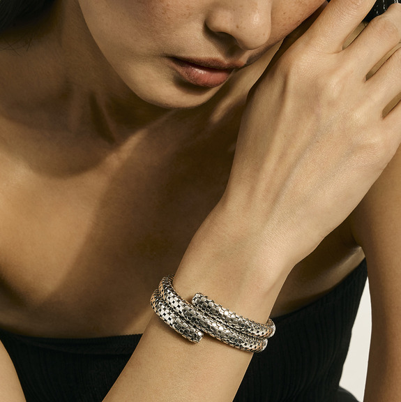 Woman wearing a textured silver bracelet on wrist, posed against a neutral background.