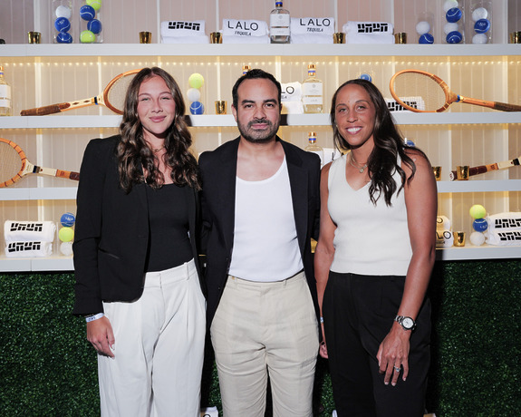 Three people posing in front of a display with tennis rackets and tennis balls.