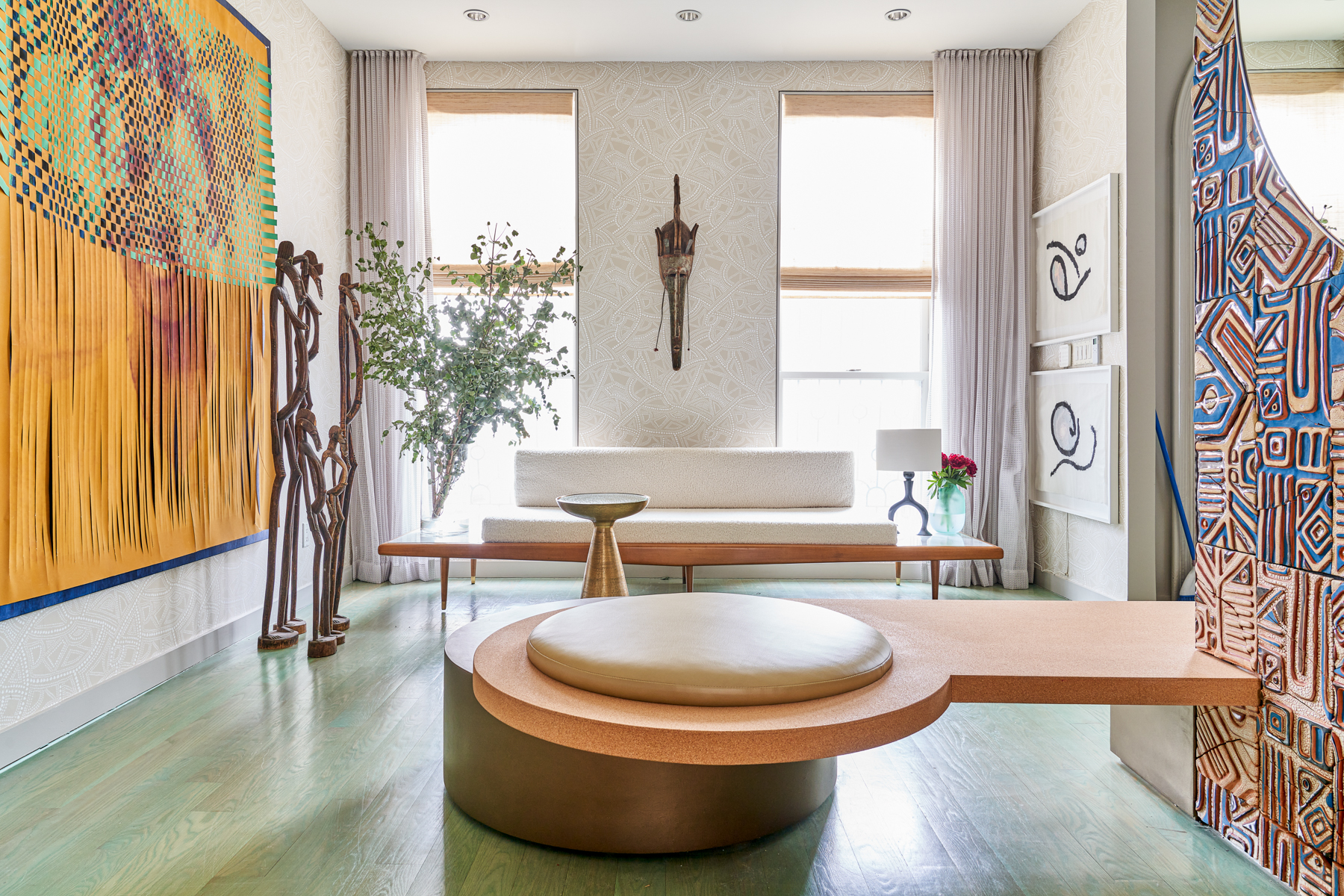 Modern living room with colorful abstract art, sculptural decor, and elegant furniture, featuring a large central round bench.
