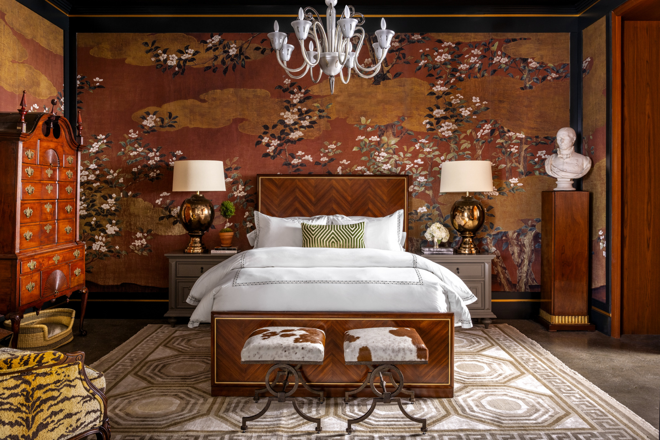 Luxurious bedroom with ornate wallpaper, elegant chandelier, wooden furniture, and decorative accents.