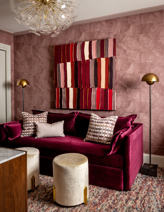 Stylish living room with red velvet sofa, colorful striped artwork, gold floor lamps, and modern decor elements.