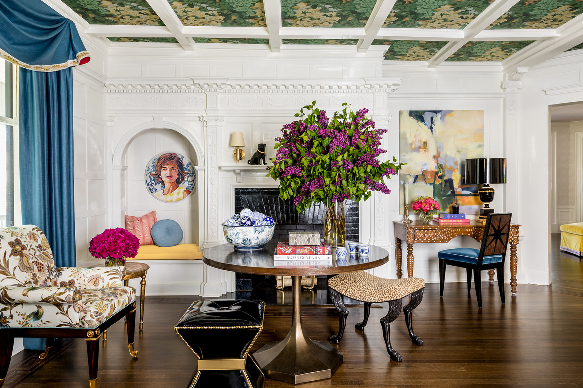Colorful living room with floral ceiling, eclectic furniture, vibrant artwork, and a large purple flower arrangement.
