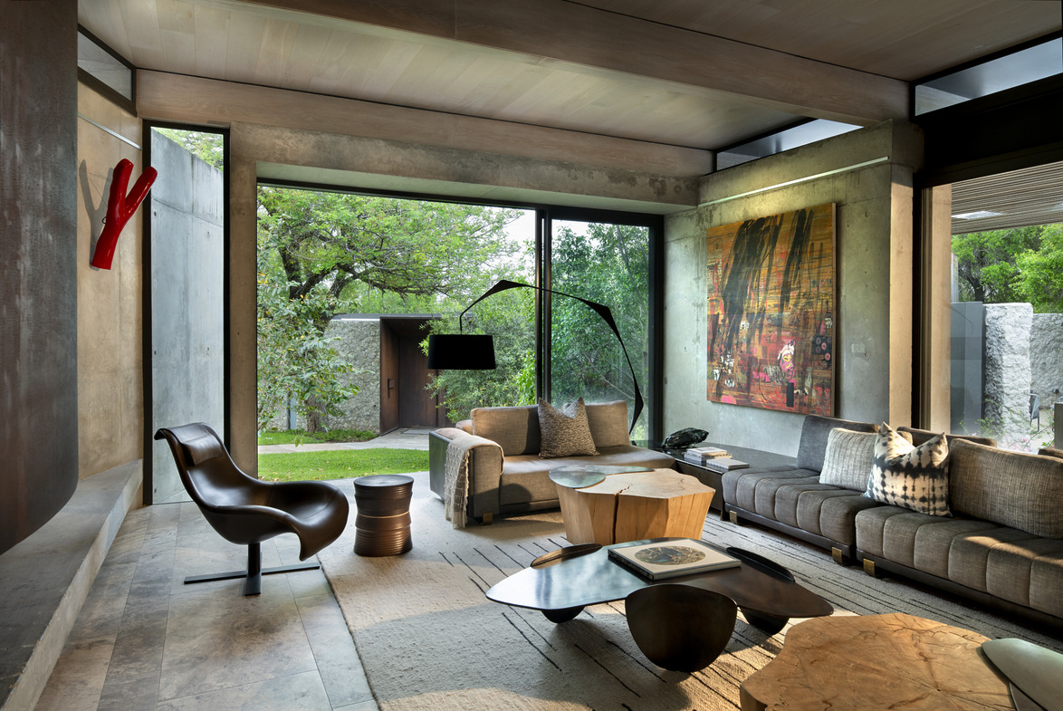 Modern living room with large windows, contemporary furniture, abstract art, and view of a lush garden.