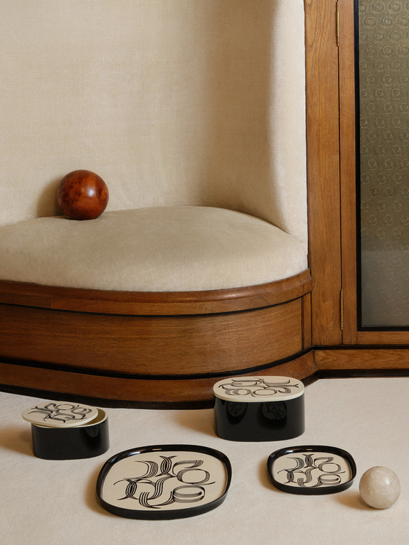 Decorative patterned trays and spherical objects on a plush bench with a wooden frame in a cozy setting.