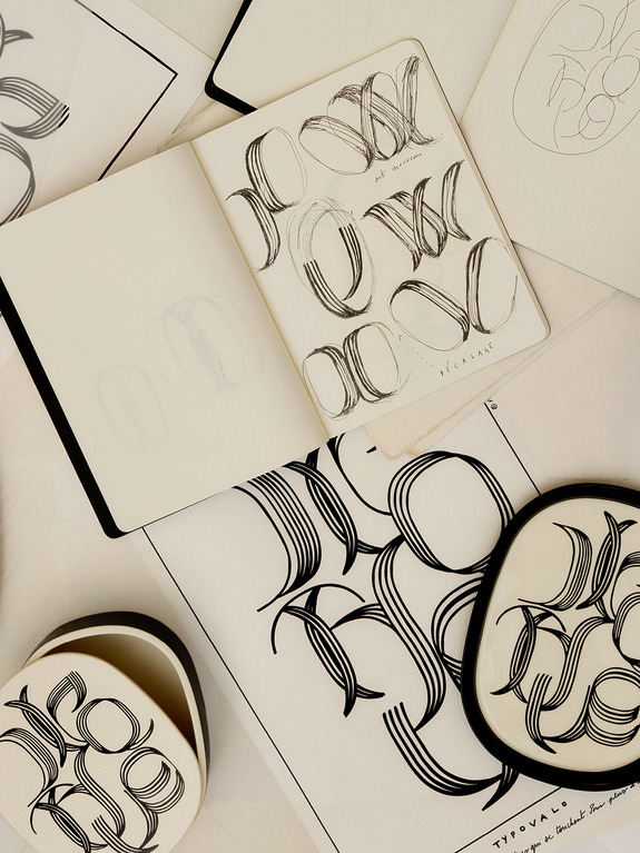 Open sketchbooks and papers displaying abstract calligraphic designs on a table.