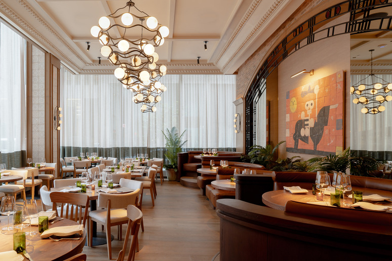 Elegant restaurant interior with modern chandeliers, wooden furniture, and art on the walls, tables set for dining.