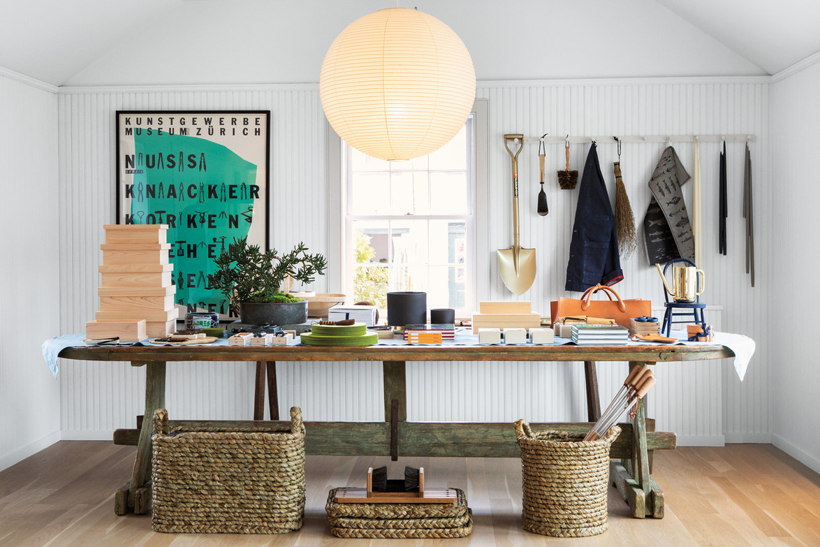 Well-organized crafts workspace with long wooden table, hanging tools, baskets, and decorative elements in a bright room.