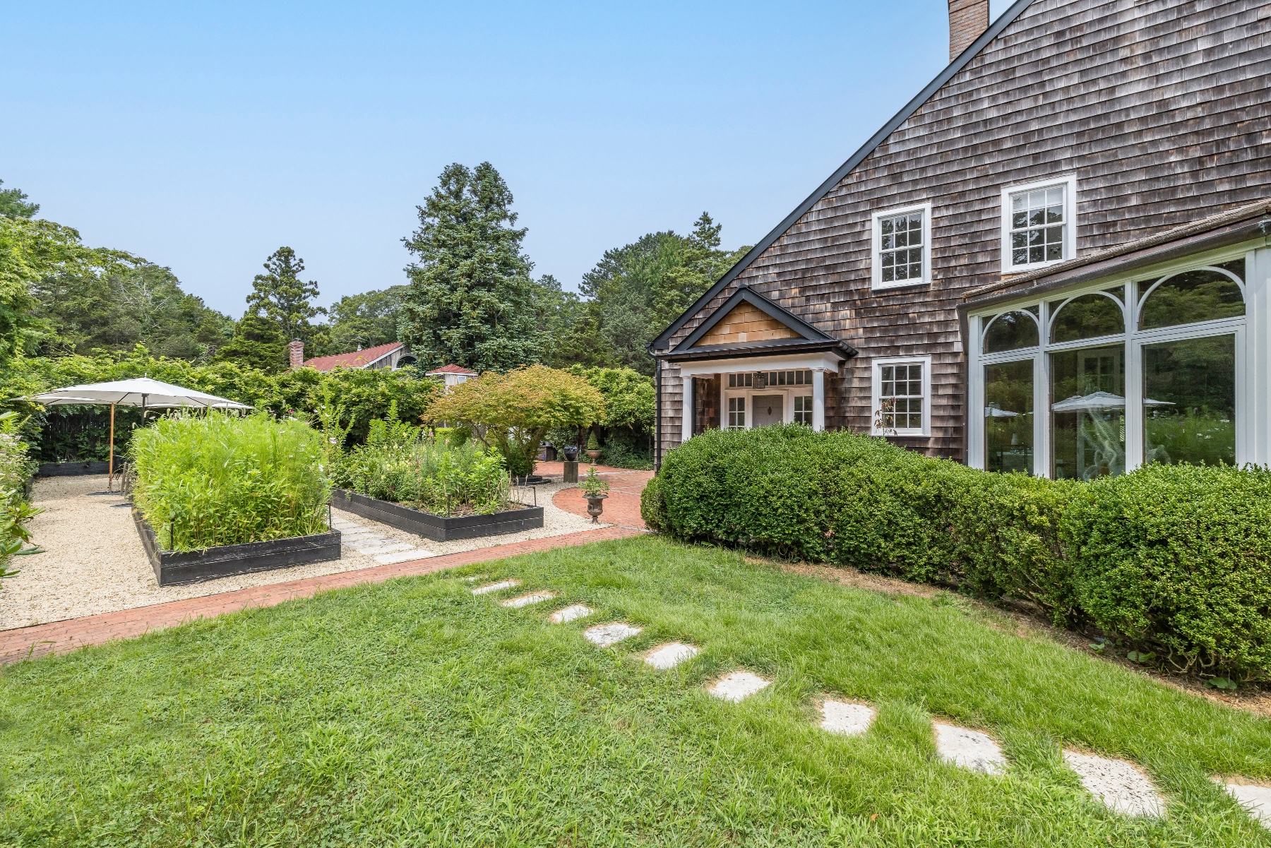 Charming house with shingle siding, lush garden, and stepping stone path on a sunny day.