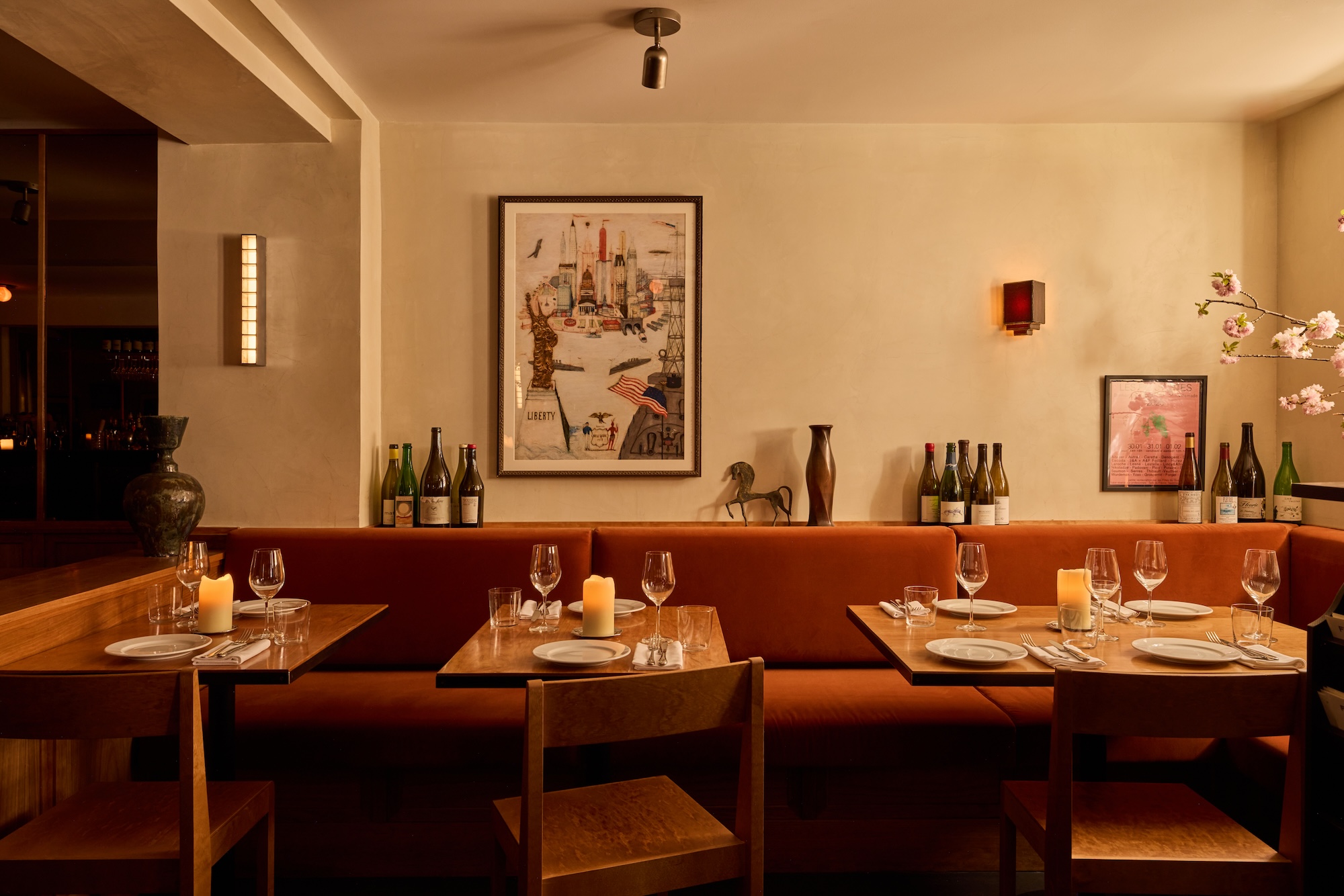 Cozy restaurant interior with tables set for dining, warm lighting, wine bottles on shelves, and artwork on the wall.