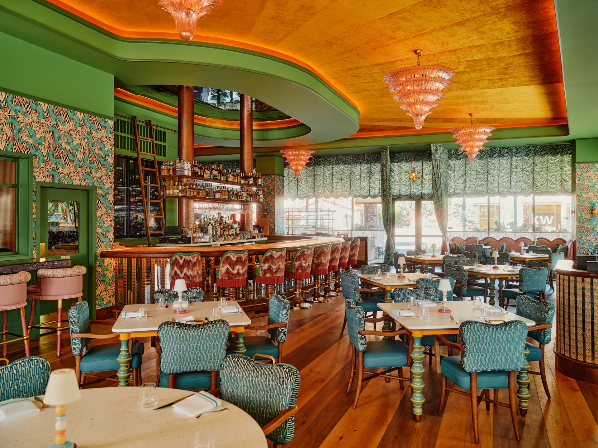 Colorful restaurant interior with patterned walls, vibrant furniture, warm lighting, and a bar area in the background.