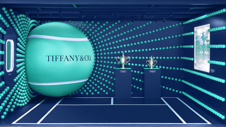 Tiffany & Co. tennis-themed display with large tennis ball and two trophies on pedestals against a vibrant dotted backdrop.
