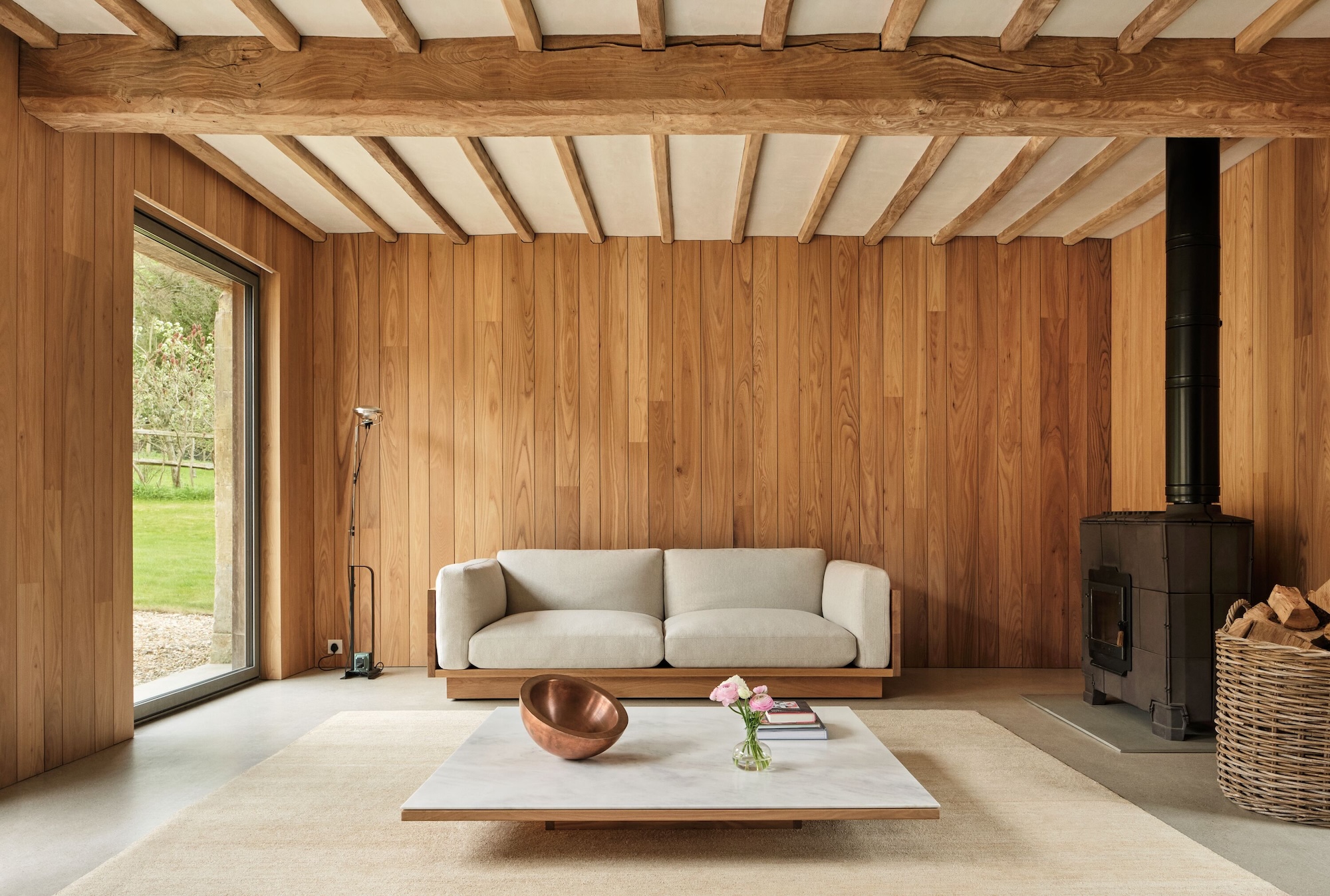 Modern rustic living room with wooden walls, a beige sofa, a fireplace, and a minimalist coffee table with decor.