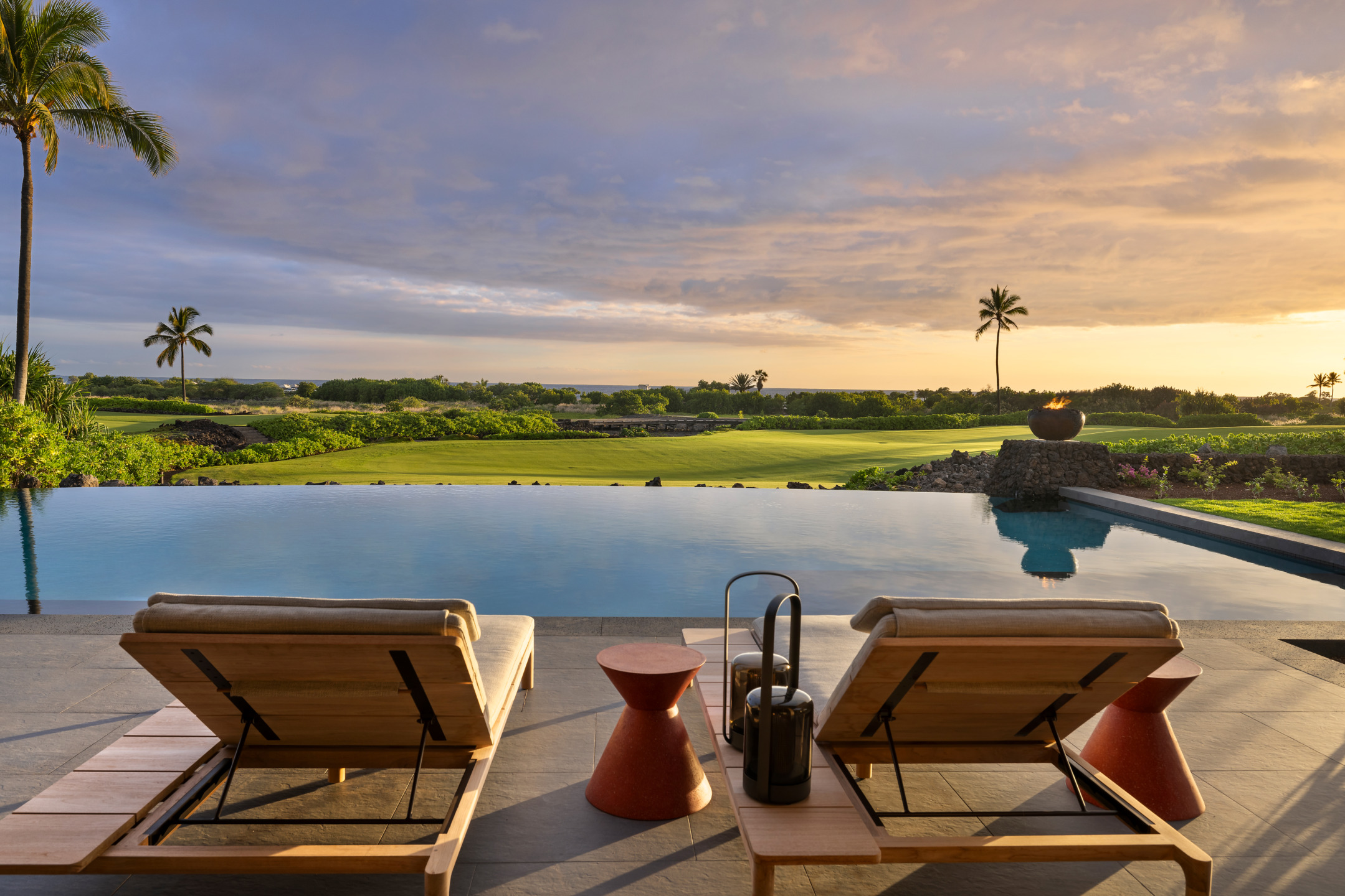 Infinity pool overlooking a scenic golf course at sunset with palm trees and two lounge chairs in the foreground
