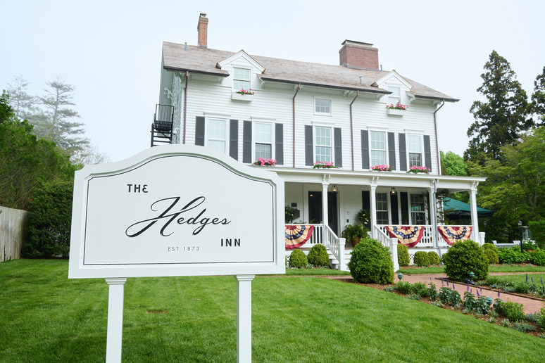 White historic inn with greenery, flower boxes, and a large sign reading "The Hedges Inn Est 1873" in the foreground.