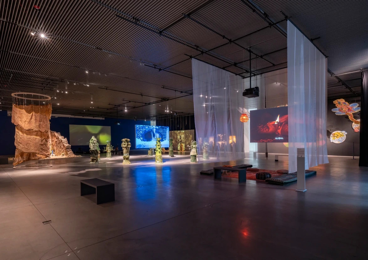 Modern art museum exhibit with sculptures, digital screens, and ambient lighting in a spacious, dimly lit room.