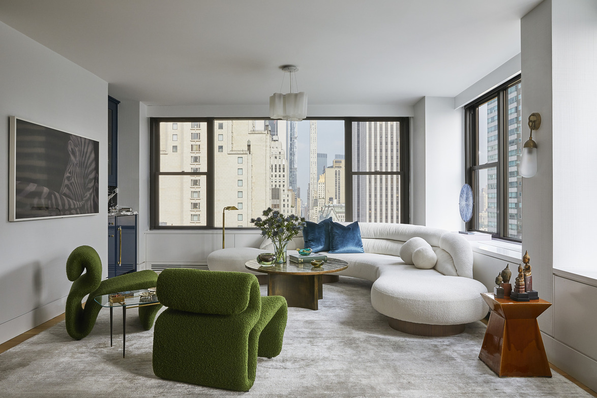 Modern living room with green chair, round white sofa, large windows overlooking cityscape, and stylish decor.