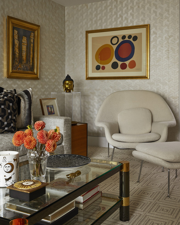Modern living room with abstract art, patterned wallpaper, and a cozy chair with matching ottoman.