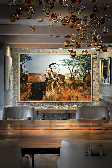 Dining room with a large wooden table, modern chandelier, and wildlife-themed painting on a stone accent wall.