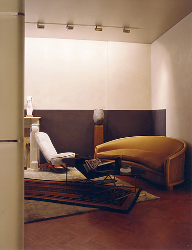 Cozy living room with a modern curved sofa, armchair, coffee table, rugs, and wall lighting.