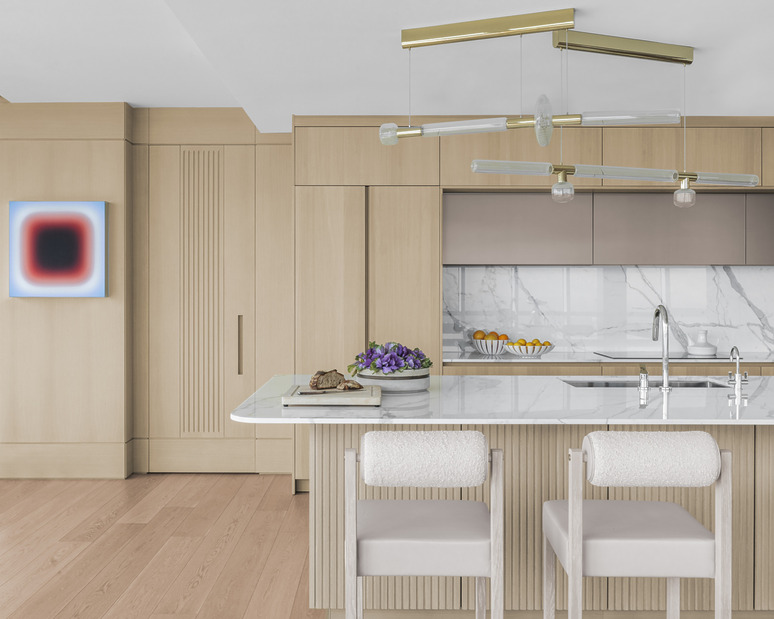 Modern kitchen with light wood cabinetry, marble countertops, two chairs, and contemporary lighting fixtures.