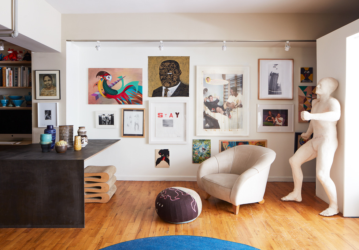 Eclectic art gallery wall in a modern living room with a sculpture, beige chair, and wooden floor.