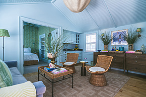 Cozy living room with wicker chairs, green accents, table with decor, and view into a bright bedroom.
