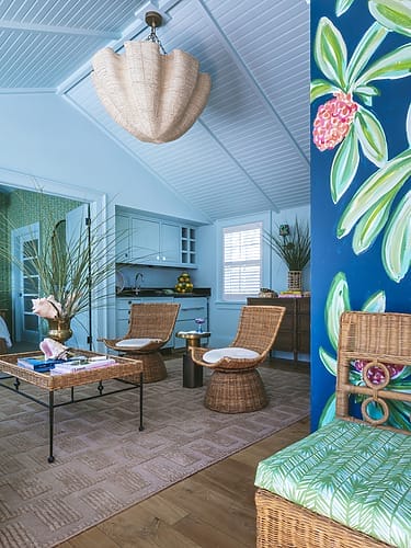 Colorful room with tropical decor, wicker furniture, and a vibrant mural. Bright blue walls and ceiling with natural light.