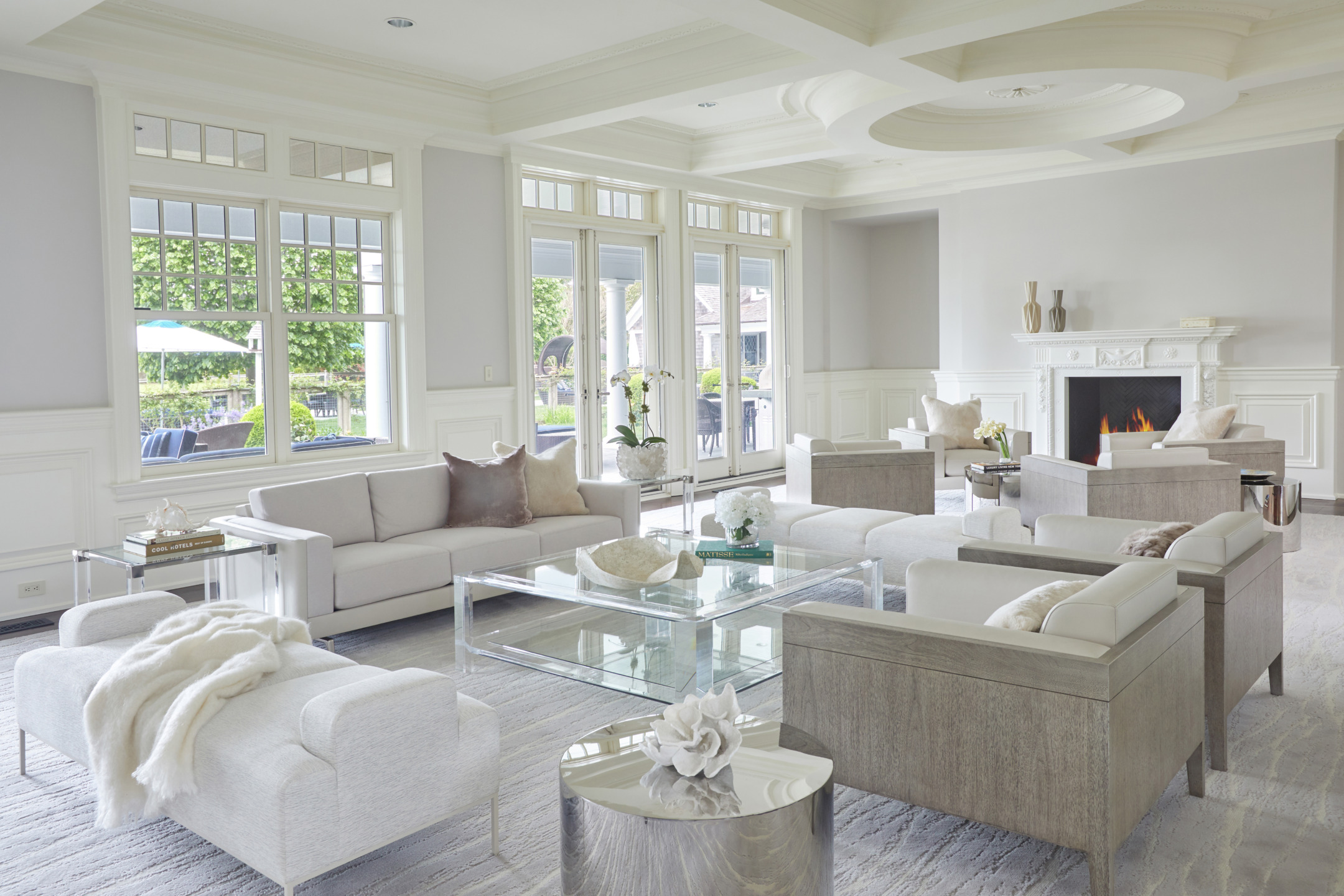 Bright living room with white furniture, glass coffee table, modern decor, large windows, and a cozy fireplace.