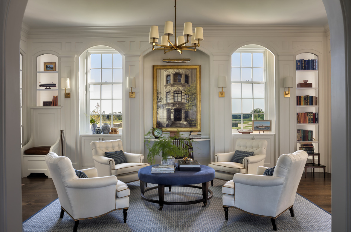 Elegant living room with four white armchairs around a blue coffee table, large windows, and a chandelier.