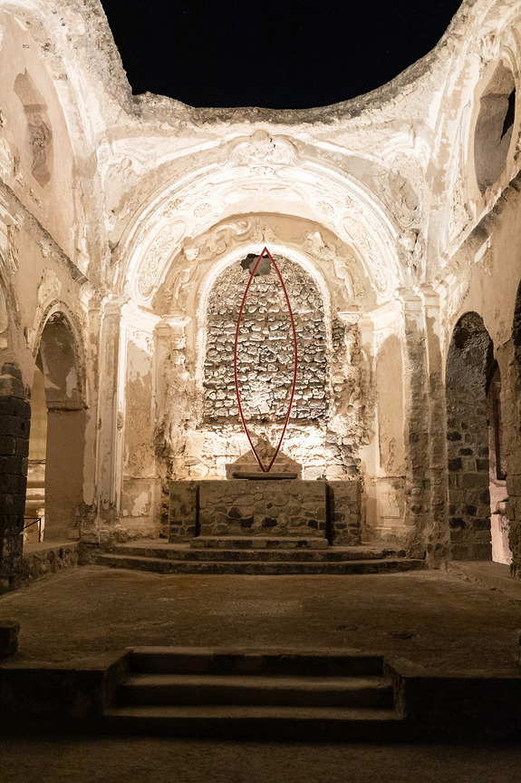 Ancient stone structure with arches and a central red sculpture, dimly lit interior with intricate carvings.