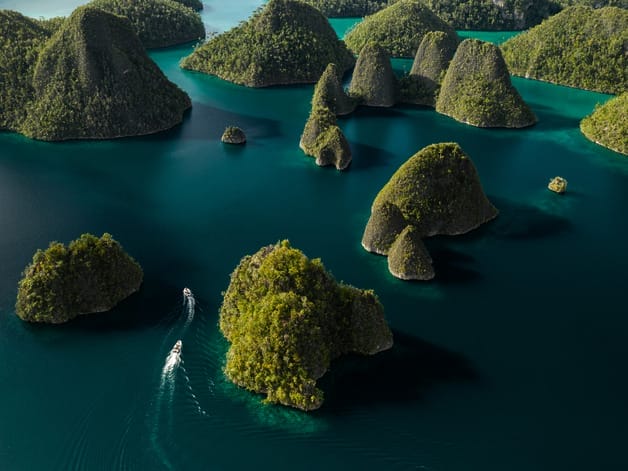 Aerial view of green islands with lush vegetation surrounded by clear blue water, showcasing natural beauty.