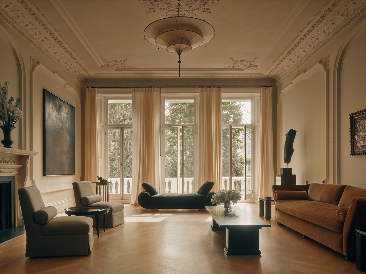 Elegant living room with large windows, vintage furniture, ornate ceiling, and art pieces, creating a sophisticated atmosphere.